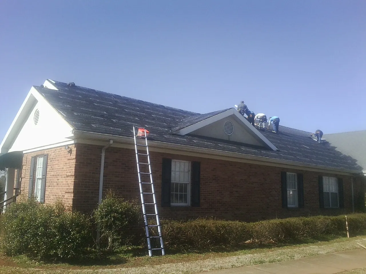 Crew tearing shingles off a brick ranch roof with a ladder set — Metal Roof Repair work by our crew in Roslyn