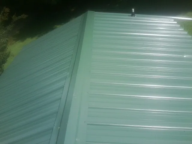New green metal panels meeting at the ridge of a roof — Flat Roof Repair work by our crew in Roslyn