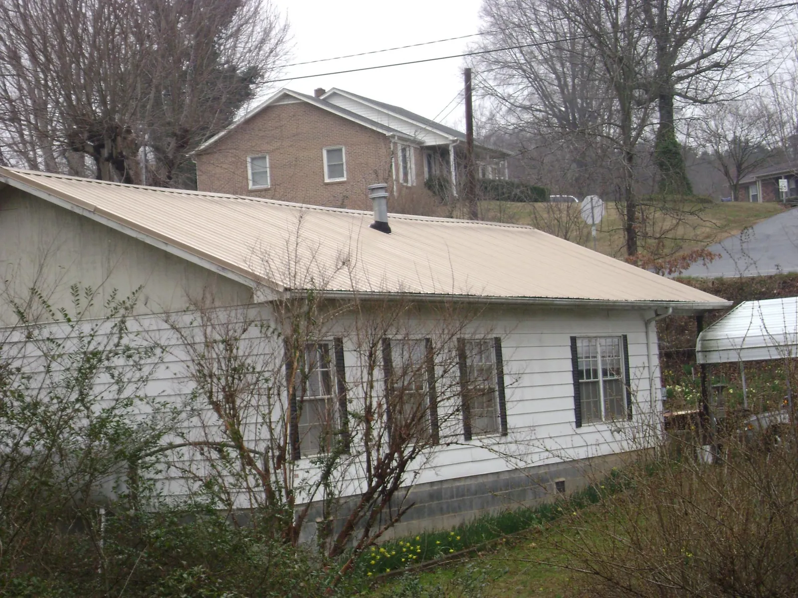 Tan metal roof on a white sided house set into a hillside — Commercial Roofing by Roofing Brothers in Roslyn